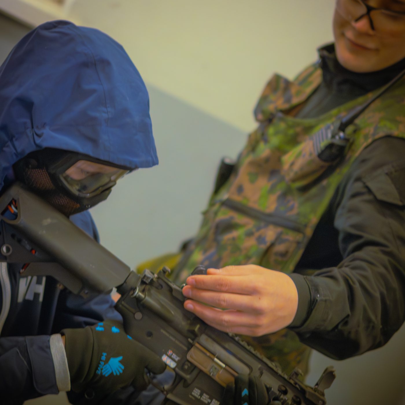 Pelinvetäjä opastaa nuorta pelaajaa airsoft-replikan käytössä sisäpelialueella
