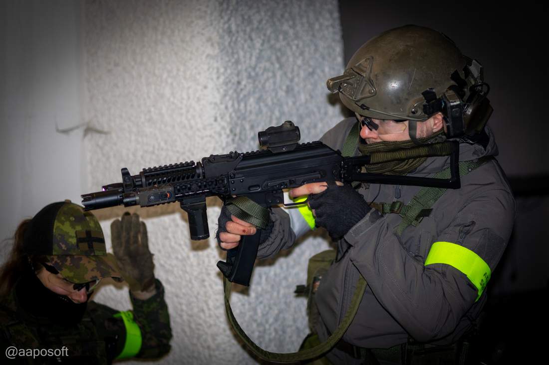 Kylmis-pelipaikka — kaksi airsoft-pelaajaa luokkahuoneessa, etummainen ampuu replikalla, taustalla valkoinen seinä